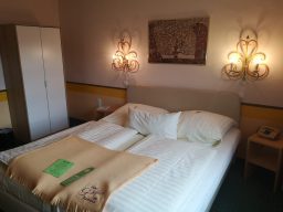 Helle Hotelzimmer mit Doppelbett, Nachttischen und einem Kasten im Hintergrund.