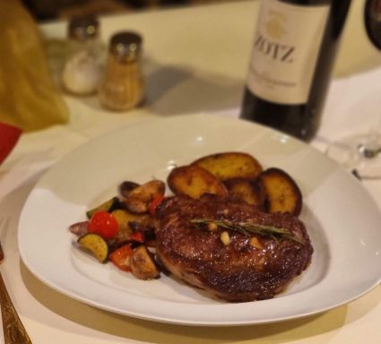 Ein saftiges Steak mit gerösteten Kartoffeln und Gemüse, neben einer Weinflasche.