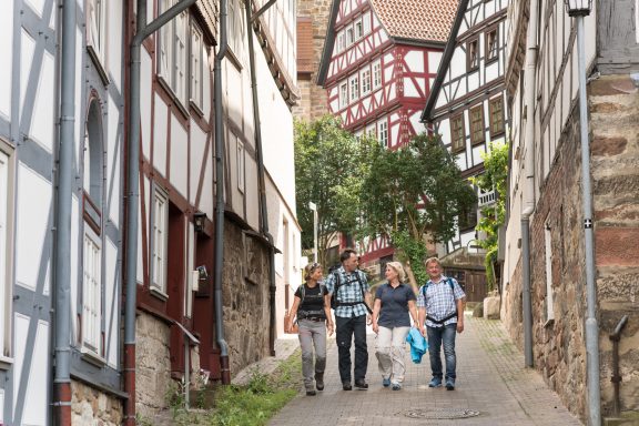 Vier Personen gehen eine schmale Straße zwischen historischen Häusern entlang.