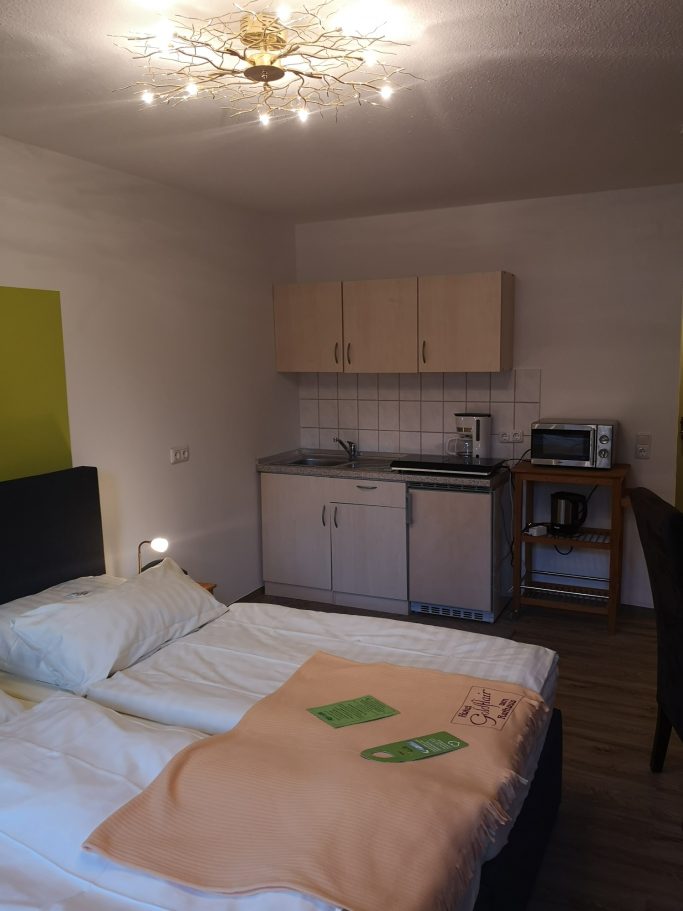 Helles, modernes Zimmer mit Doppelbett, kleiner Küchenzeile und Tisch.