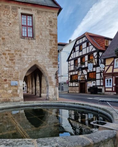 Historisches Stadtbild mit Brunnen, Fachwerkhäusern und einer steinernen Bögen.