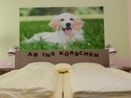 Ein helles Schlafzimmer mit einem Hunde-Motiv über einem Doppelbett und gelber Bettwäsche.