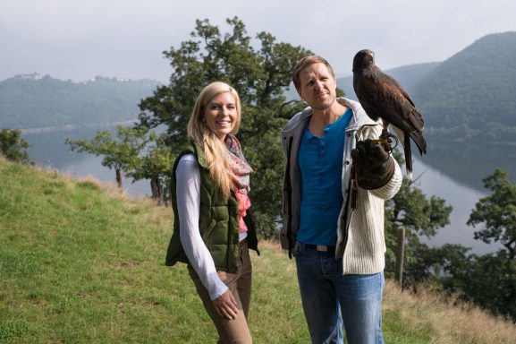 Paar steht auf einer Wiese am Wasser und hält einen Adler auf einem Handschuh.