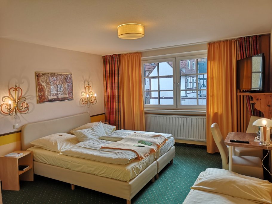 Helles Hotelzimmer mit zwei Betten, Tisch und Fenster mit Blick nach draußen.