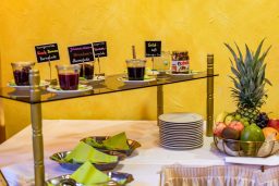 Buffet mit verschiedenen Getränken, Marmelade und frischem Obst auf einem Tisch.