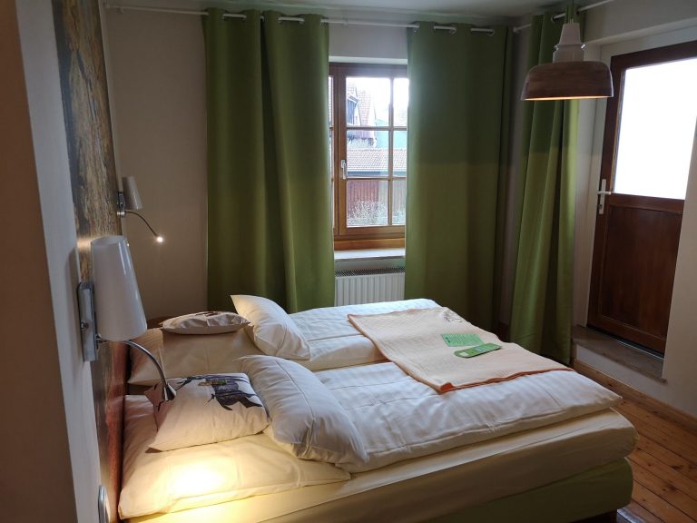 Helle Schlafzimmer mit zwei Betten, grünen Vorhängen und einem Fenster.