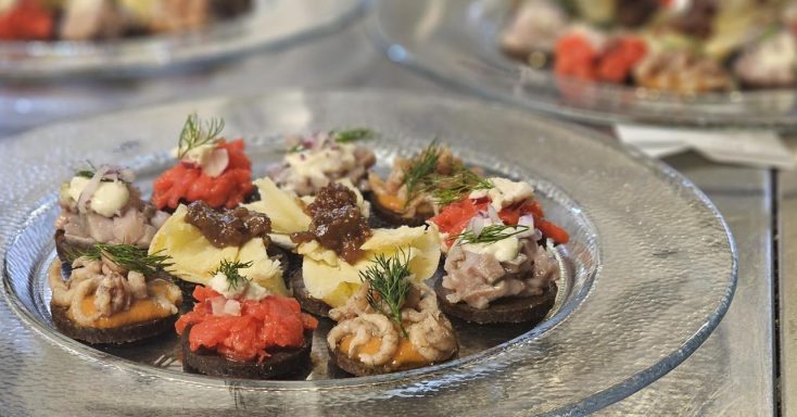 Bunte Häppchen auf einem Glasplatten, dekoriert mit frischen Kräutern und Gemüsestücken.