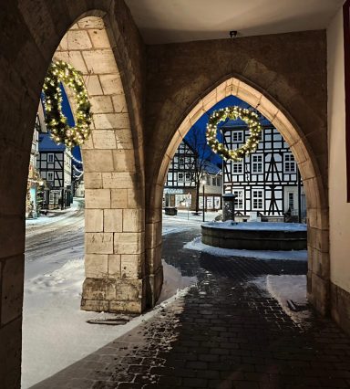 Historischer Torbogen mit Blick auf ein verschneites Fachwerkhaus und Weihnachtskränze.
