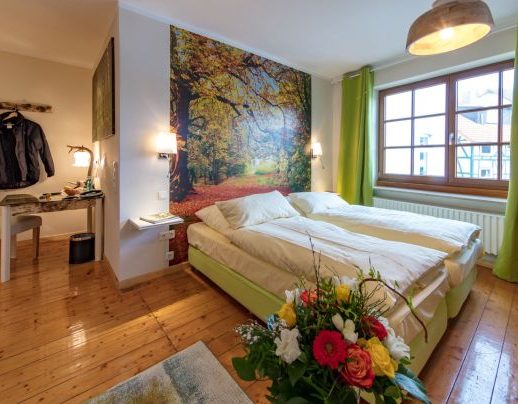 Helles Schlafzimmer mit zwei Betten, einer Blumenarrangement und einer Wandmalerei von Bäumen.