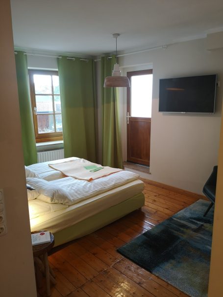 Helles Schlafzimmer mit Doppelbett, Holzfußboden und Zugang zu einem Balkon.