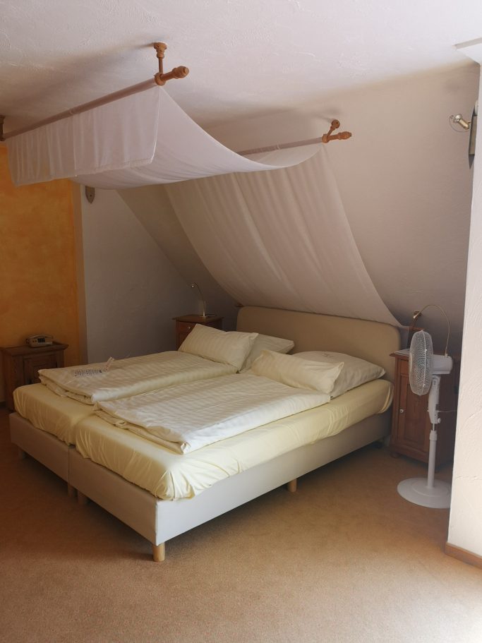 Ein Schlafzimmer mit einem Doppelbett, leichtem Stoffdach und einem Ventilator.