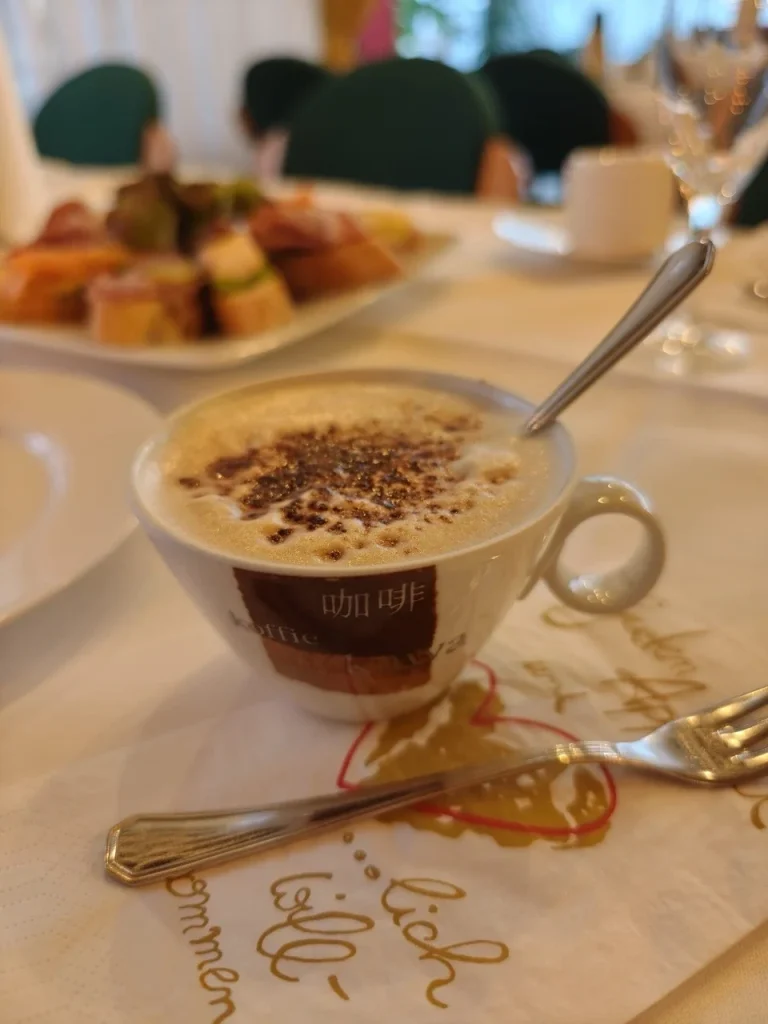Tasse mit Cappuccino, dekoriert mit Schokoladenstreuseln, auf einem gedeckten Tisch.