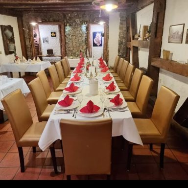 Gedeckter Tisch mit weißen Tischtüchern und roten Servietten in einem rustikalen Restaurant.