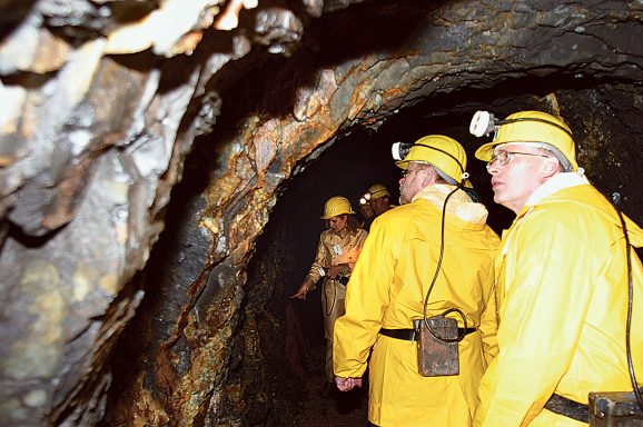 Gruppe von Personen in gelber Schutzkleidung und Helmen in einem dunklen Tunnel.