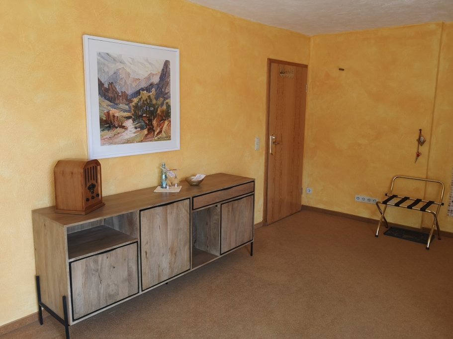 Heller Raum mit gelber Wand, Holzmöbeln, einem Gemälde und einer Tür.