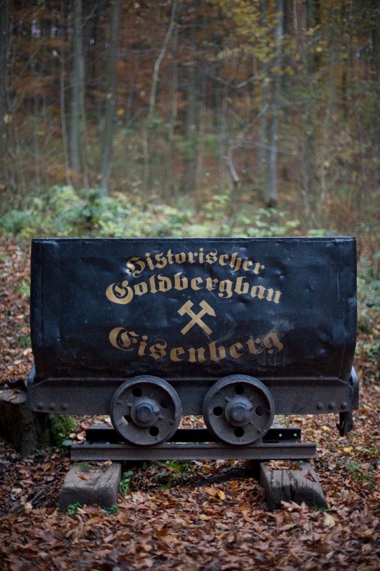Historische Lore der Goldbergbahn Eisenberg im Wald, mit goldener Schrift und zwei Rädern.