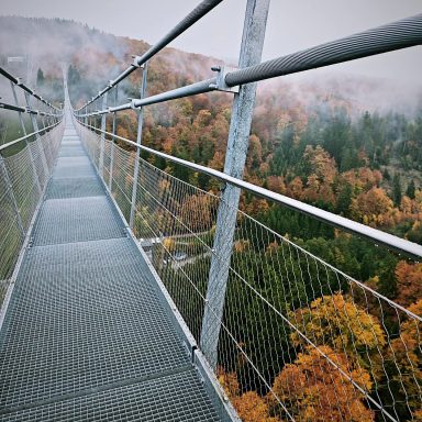 Schwebende Hängebrücke über herbstliche Wälder im Nebel.