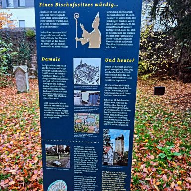 Info-Tafel mit historischen Details und Bildern in herbstlicher Umgebung.