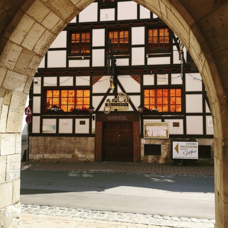 Fachwerkhaus mit beleuchteten Fenstern, gesehen durch einen alten Torbogen.