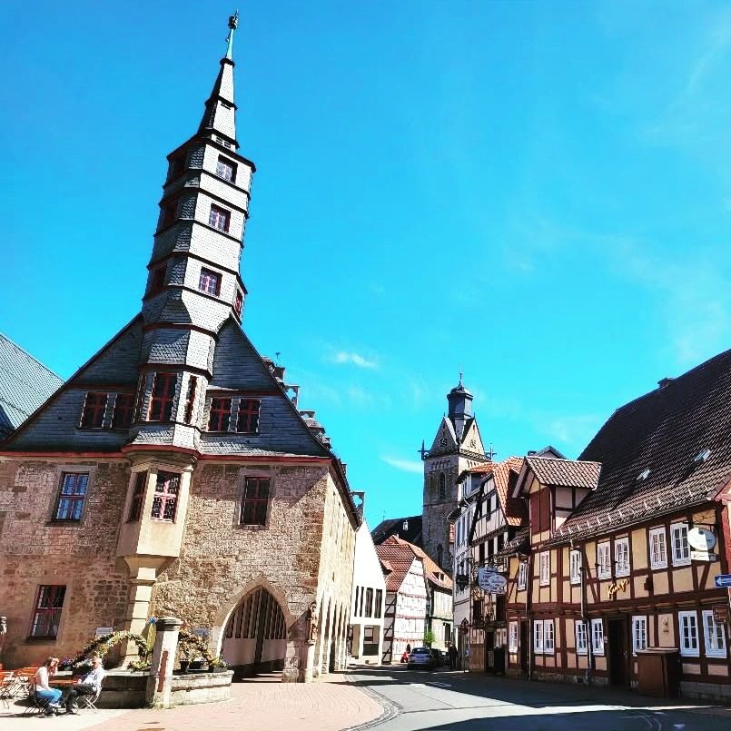 Historische Gebäude mit Fachwerk und einem spitzen Turm unter blauem Himmel.