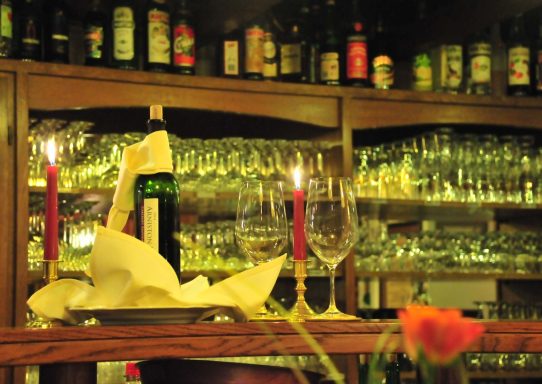 Ein Tisch mit Kerzen, Weinflasche, Gläsern und gehobener Restaurantatmosphäre.