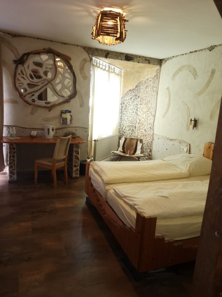 Helles Zimmer mit zwei Betten, einem Tisch und einem dekorativen Spiegel.