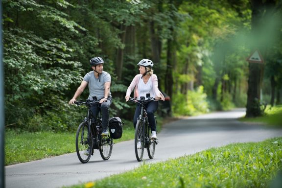 Zwei Radfahrer auf einem Waldweg, umgeben von grüner Natur.