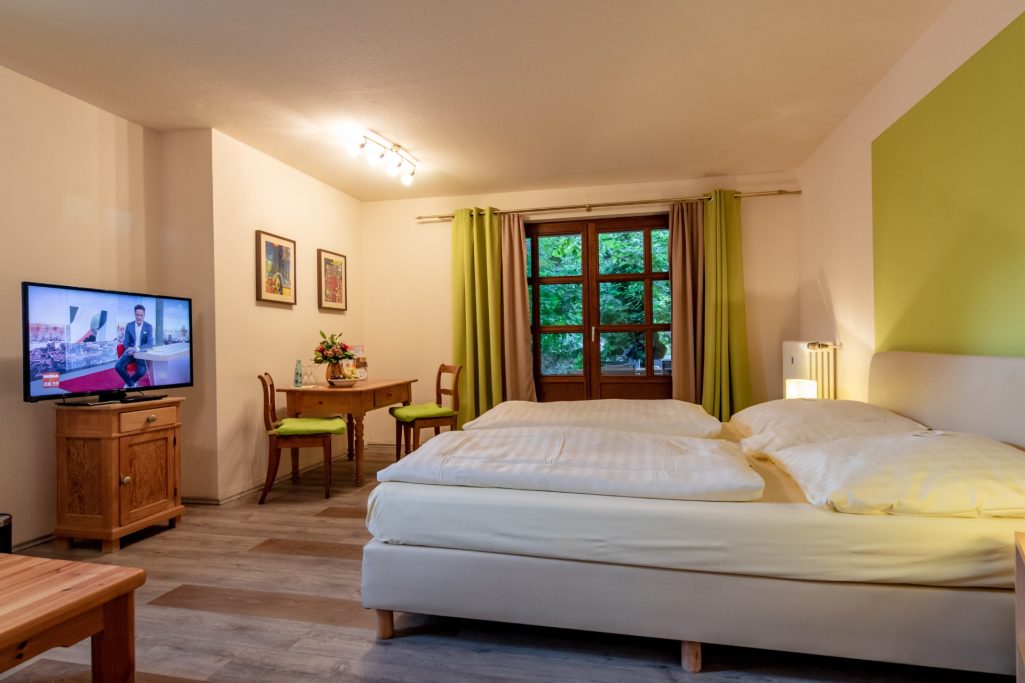 Helles Zimmer mit Doppelbett, Tisch, Stühlen und Fenster mit Blick auf die Natur.