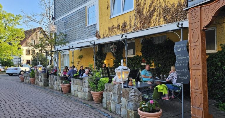 Gemütliches Café mit Gästen im Freien, umgeben von Pflanzen und Blumen.