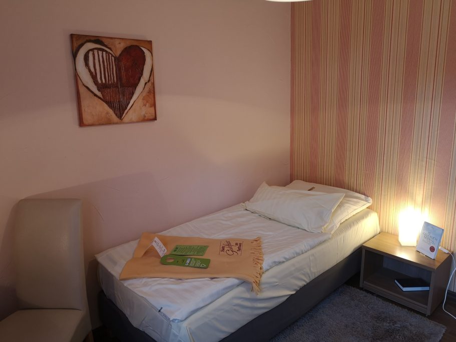 Ein einfaches Einzelzimmer mit einem Bett, Tisch, Stuhl und dekorativer Wand.