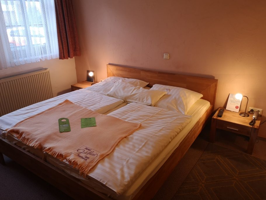 Doppelbett mit weißer Bettwäsche, Holzrahmen und sanfter Beleuchtung im Raum.