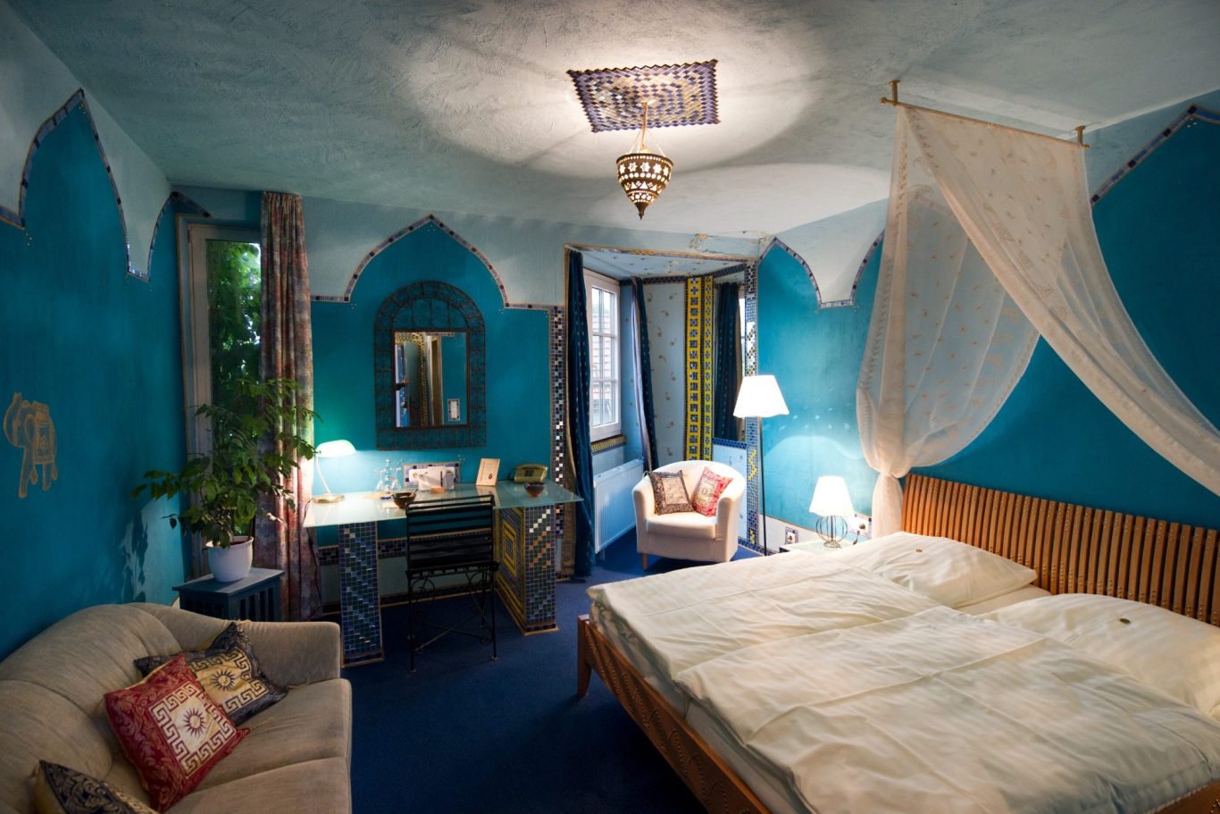 Farbige Hotelzimmer mit blauem Anstrich, Bett, Sessel und Schreibtisch.