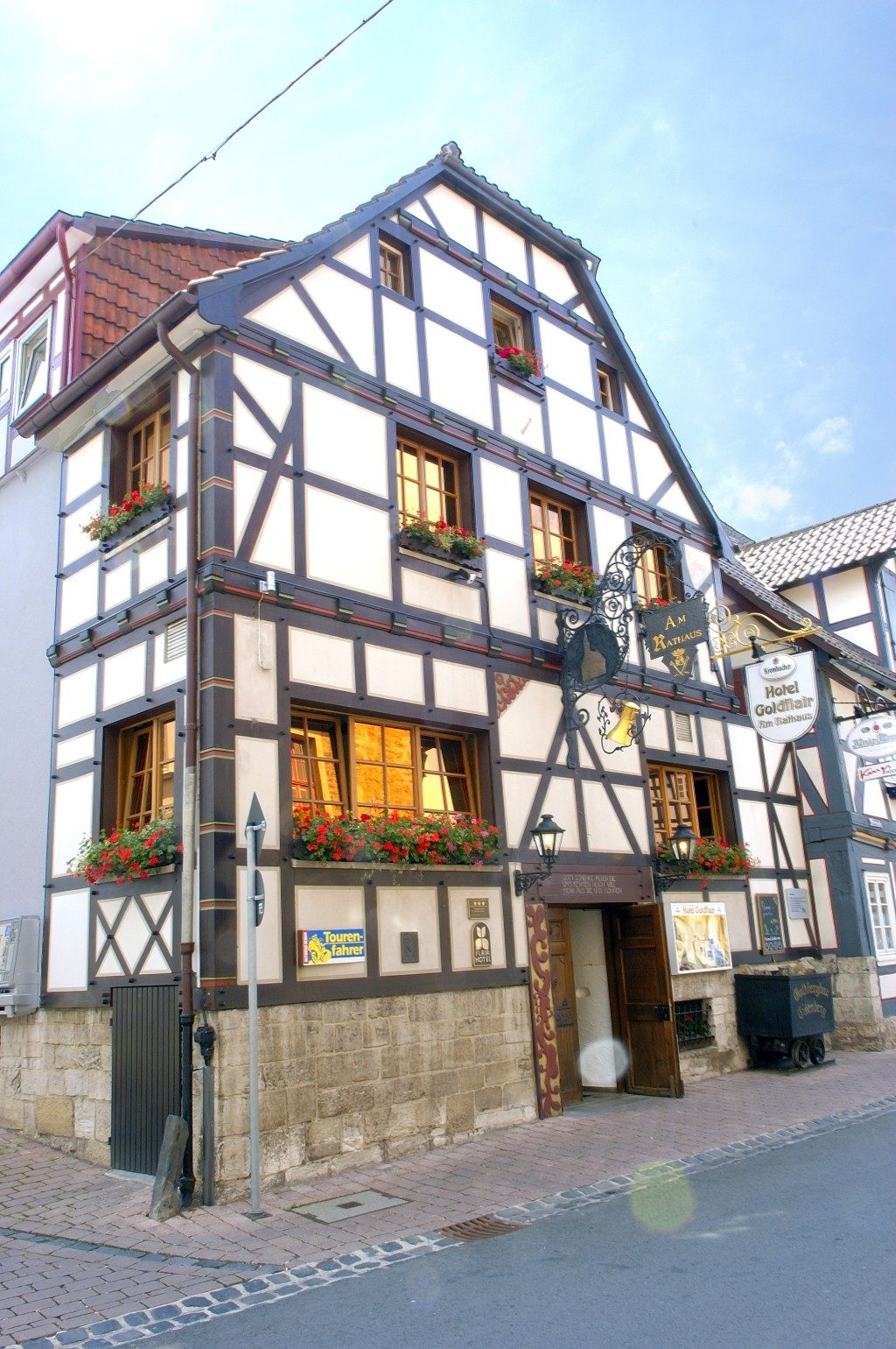 Fachwerkhaus mit weißen Wänden, dunklem Holz und blühenden Fensterkästen. Frontansicht Hotel Goldflair 