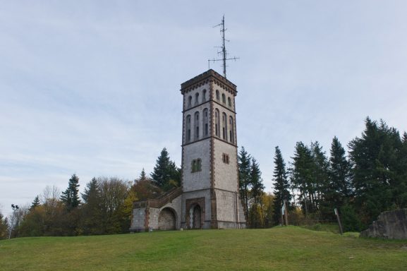 Historischer Wasserturm auf einer Anhöhe, umgeben von Bäumen.