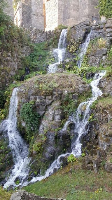 Wasserfall mit fließendem Wasser über grüne Felsen in einer naturnahen Umgebung.