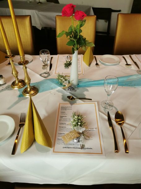 Tischgedeck mit goldenen Servietten, Rosen, Menü und Dekoration in einem eleganten Restaurant.