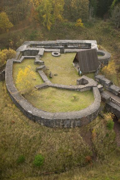Überblick auf die Überreste einer alten Festung umgeben von Bäumen und Wiese.
