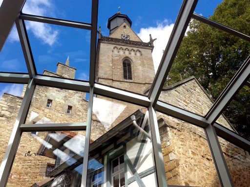 Blick durch Glas auf einen mittelalterlichen Turm und umliegende historische Gebäude.
