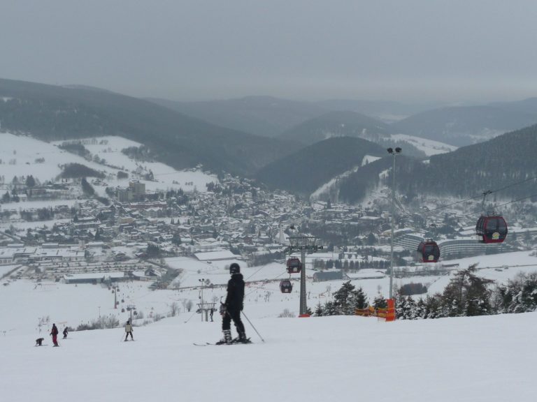 Skiende Person vor schneebedeckter Landschaft und Bergstadt, mit Seilbahnen im Hintergrund.