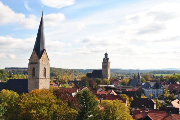 Stadtansicht mit Kirchen und buntem Laub unter einem blauen Himmel.