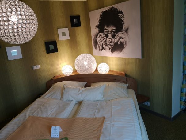 Schlafzimmer mit Doppelbett, runder Deckenleuchte und Kunstwerk an der Wand.