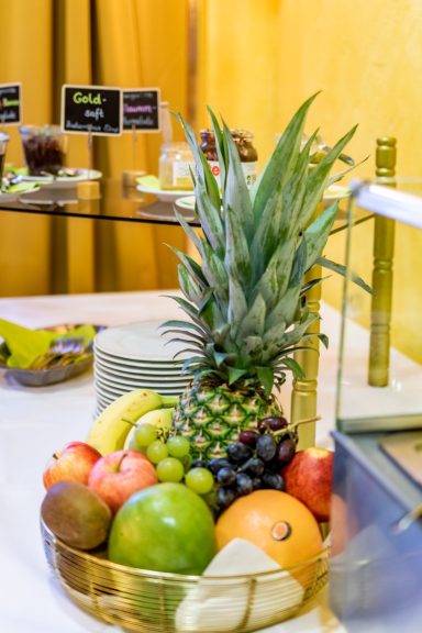 Ein Obstkorb mit Ananas, Äpfeln, Bananen, Trauben, und Orangen auf einem Tisch.