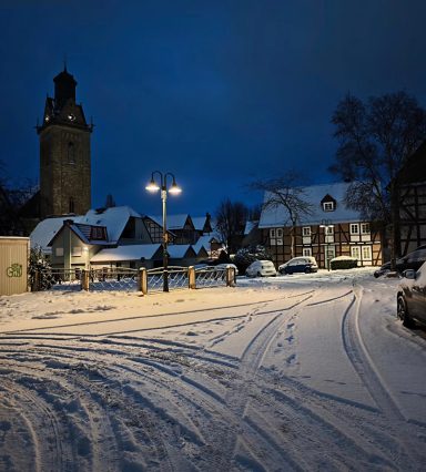 Winzige Straße im Schnee bei Nacht, beleuchtet von Straßenlaternen und einem Kirchturm.