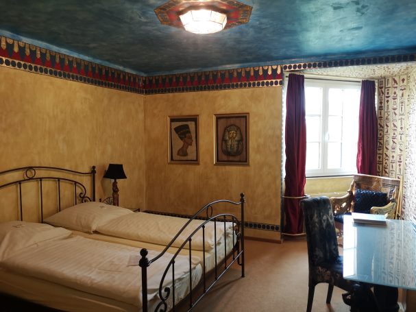 Gemütliches Zimmer mit zwei Betten, Tisch, Stuhl und dekorativen Wänden.