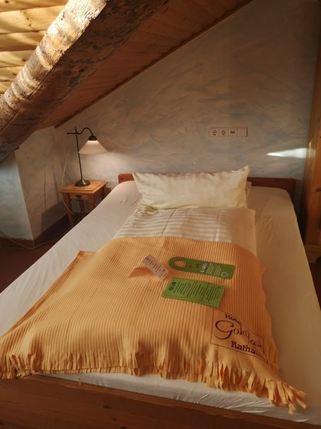 Schlafzimmer mit schrägem Dach, Bett mit orangefarbenem Bettbezug und Kissen.