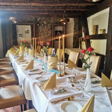 Elegant gedeckter Tisch mit goldenen Servietten, Kerzen und frischen Rosen in Vasen.