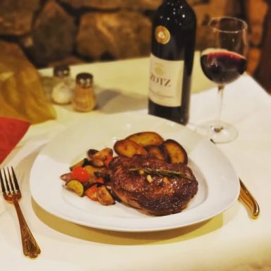 Ein dekorierter Teller mit Steak, Gemüse, Bratkartoffeln und einer Flasche Rotwein.