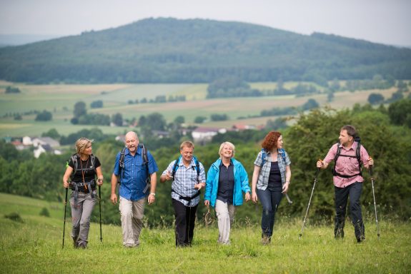Sechs Personen wandern gemeinsam auf einem Hügel, umgeben von grüner Landschaft.