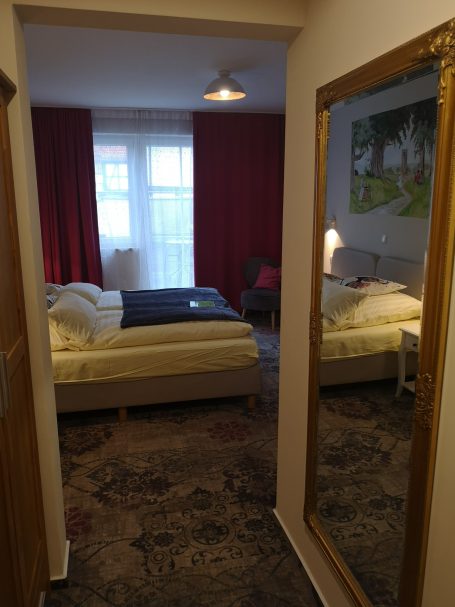 Gemütliches Zimmer mit einem Bett, einem Spiegel und roten Vorhängen.