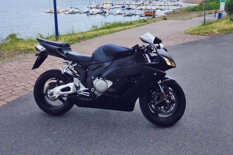 Schwarzes Motorrad parkt auf einer Straße nahe einem Hafen mit Booten im Hintergrund.